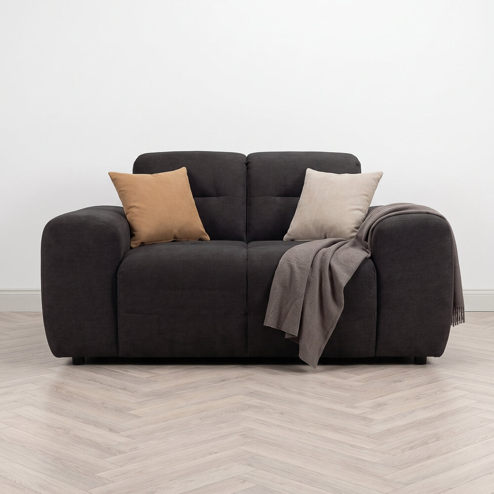 Dark fabric armchair with two throw pillows, draped blanket, and padded armrests