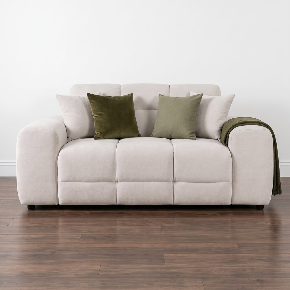 Beige 2-seater sofa with tufted seat, rounded arms, green throw and three cushions.