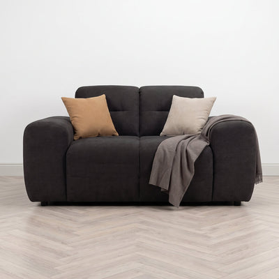 Dark fabric armchair with two throw pillows, draped blanket, and padded armrests