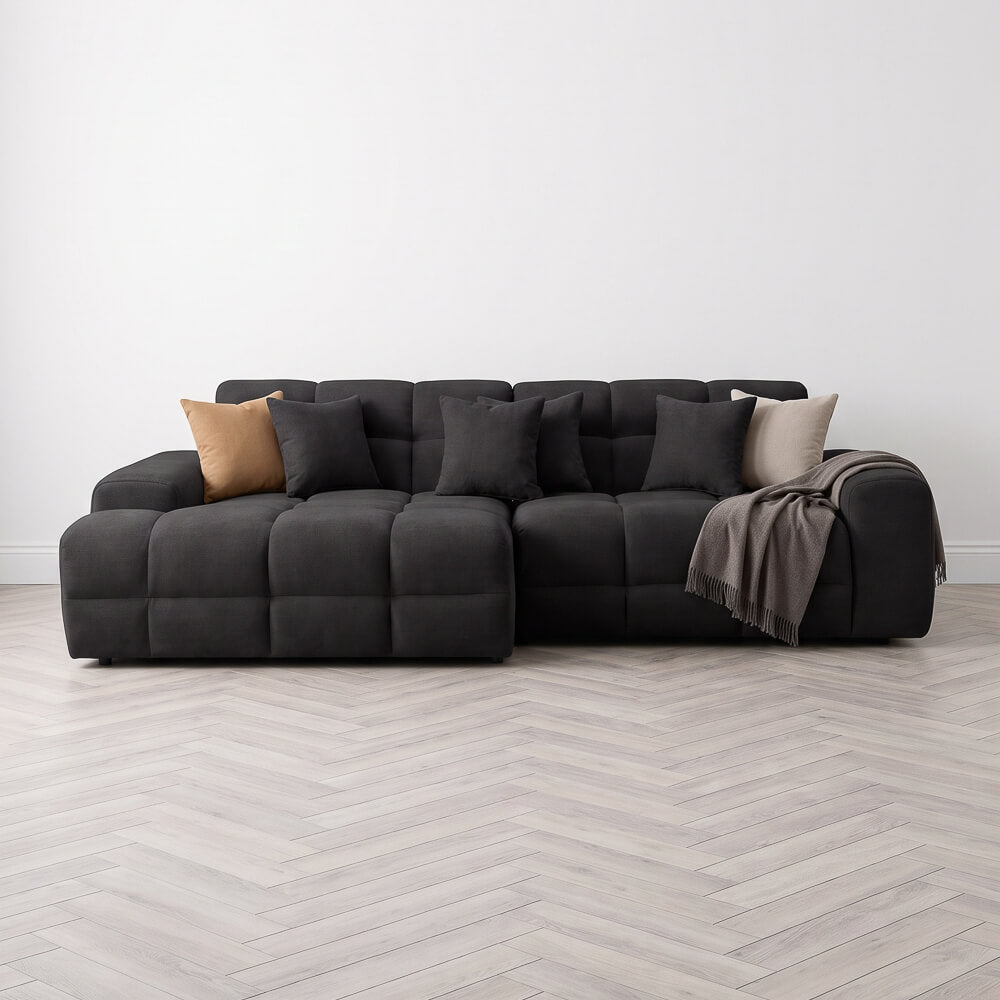 Black left corner sofa with tufted cushions, throw blanket, and accent pillow.