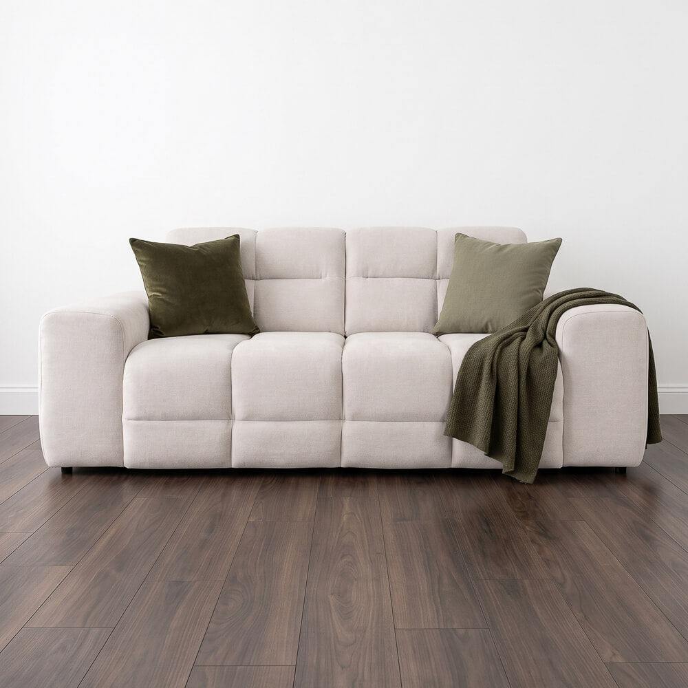 Beige three-seater sofa with two green pillows and draped throw blanket