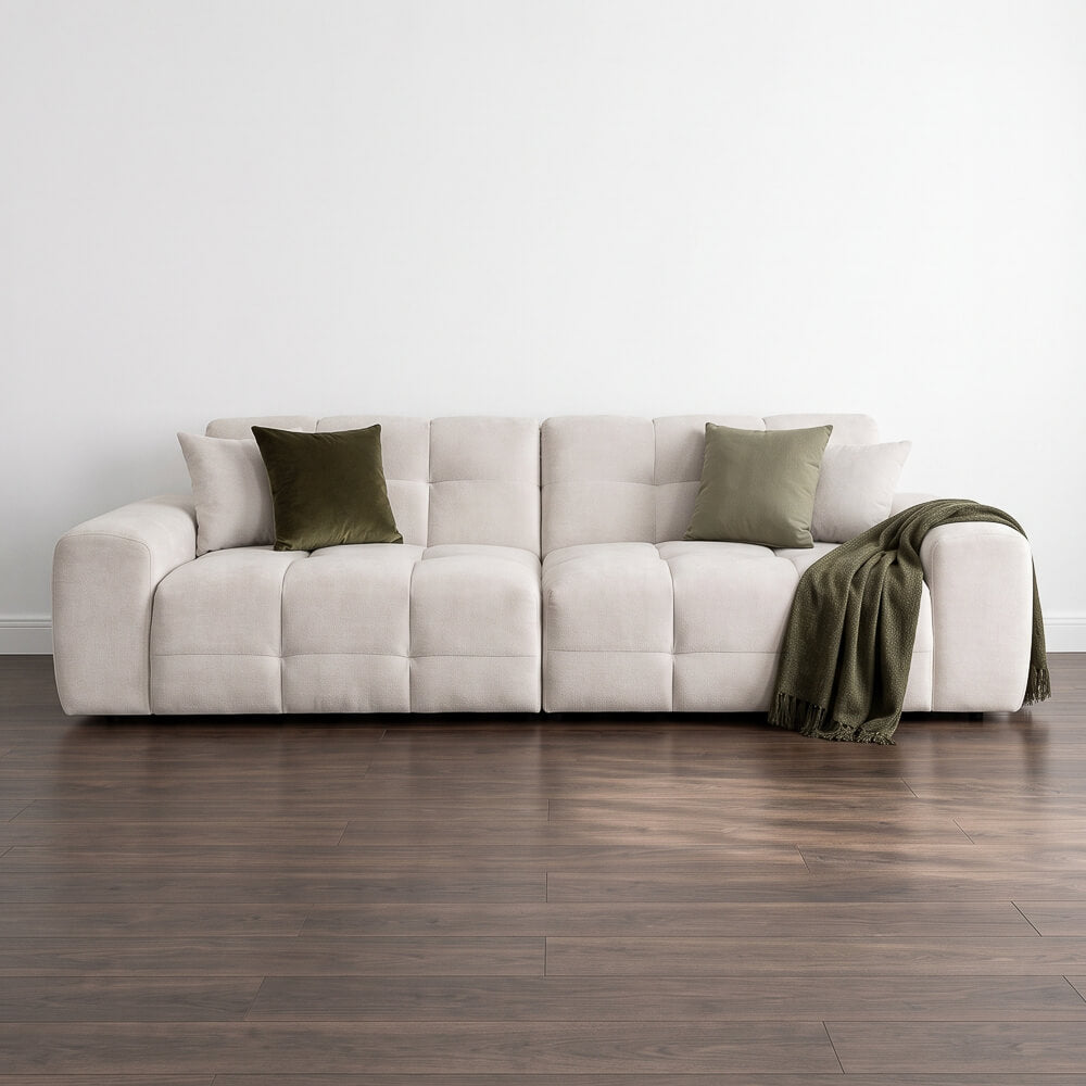 Light beige 4-seat sofa with tufted cushions, boxy arms, and accent pillows plus throw