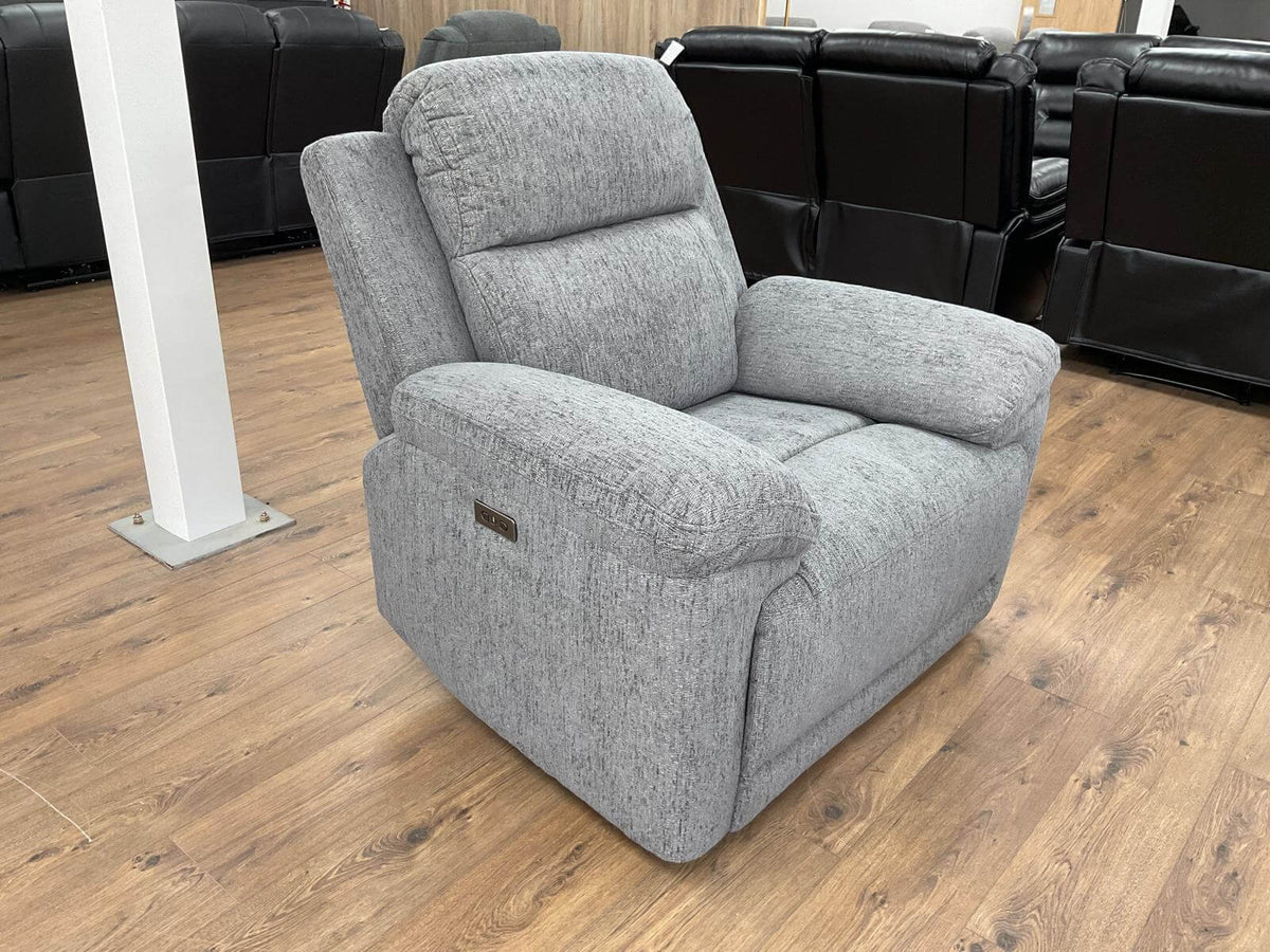 Grey fabric recliner chair angled view, padded headrest and wide armrests.
