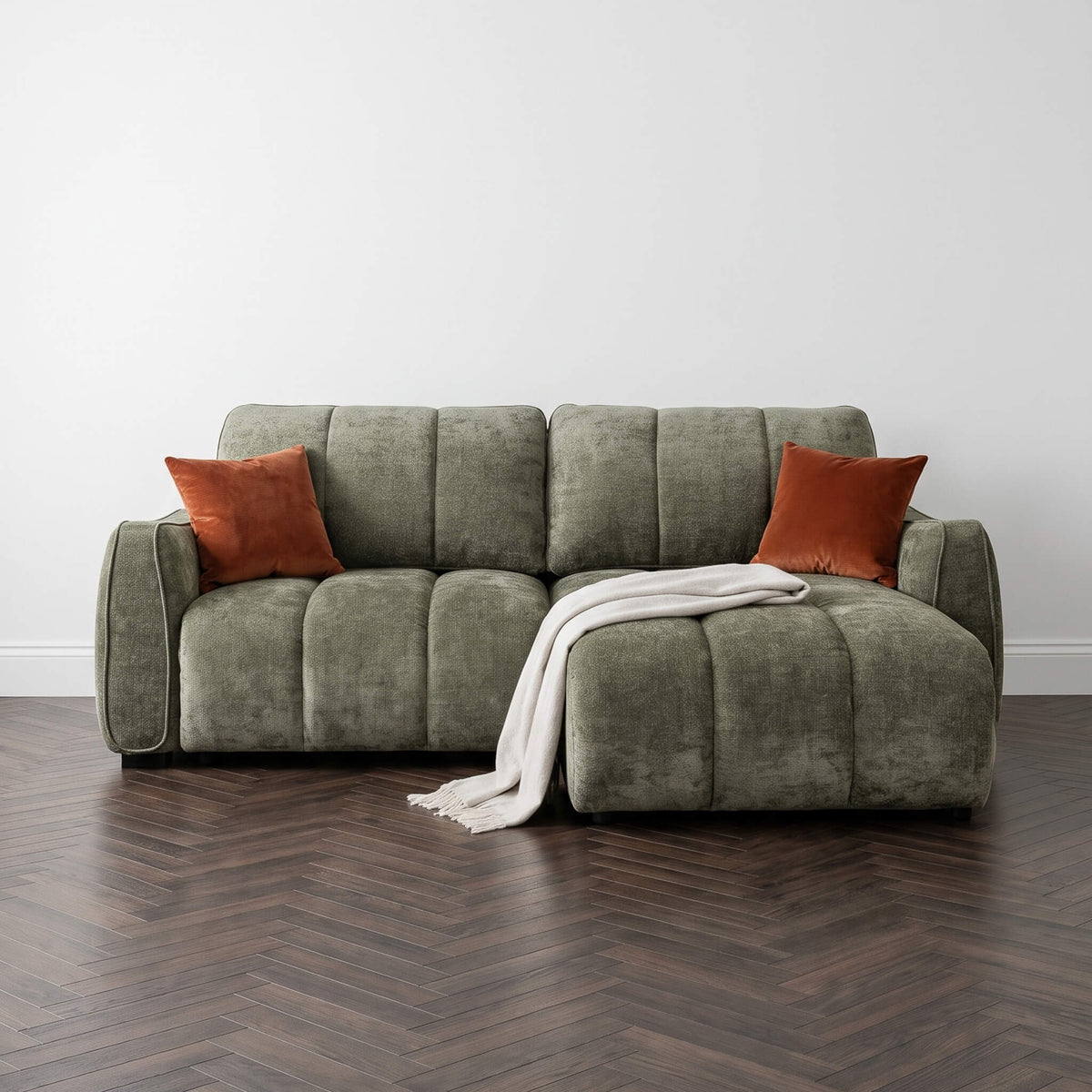 Corner sofa bed unfolded into daybed with greenish-gray cushions and two orange throw pillows