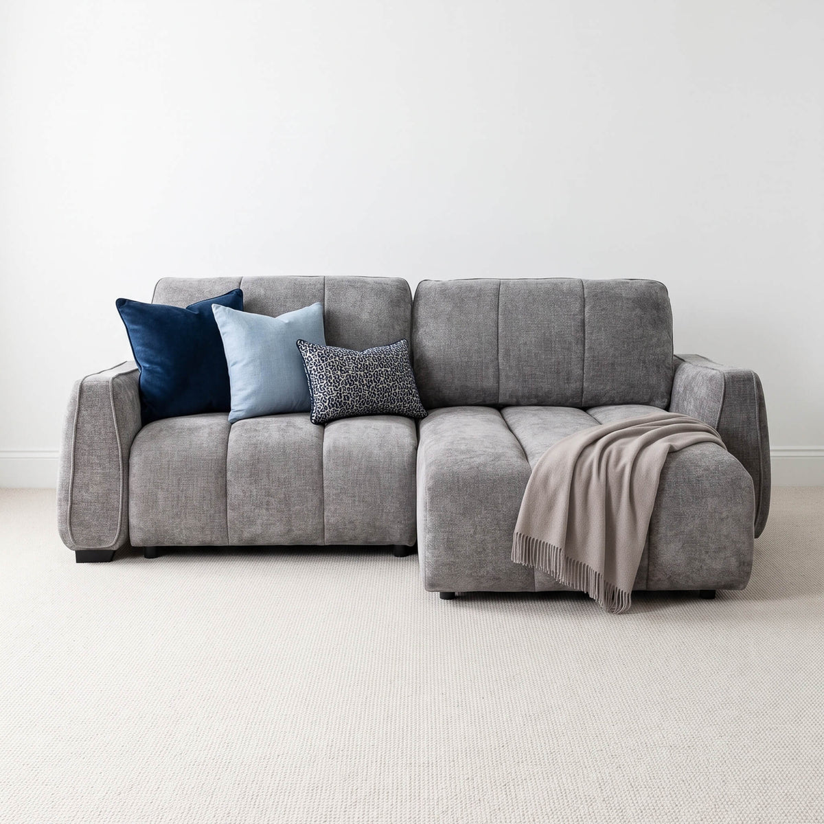 Grey corner sofa bed with chaise, blue and patterned cushions and taupe throw blanket.
