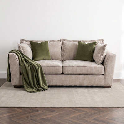 Beige 3-seater sofa with draped throw blanket and two green accent pillows
