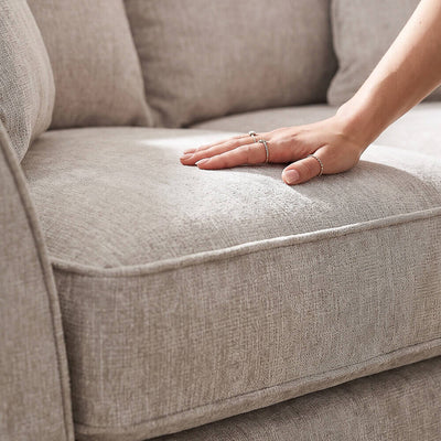 Beige sofa seat cushion with hand resting on textured upholstery fabric